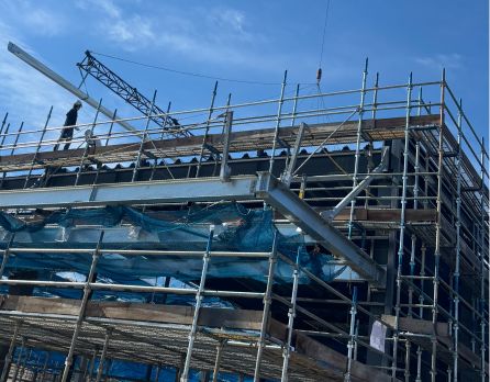 工場の屋根に板金材を持ち上げる作業