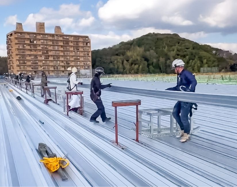 100メートルの工場屋根に板金屋根材を設置する作業風景